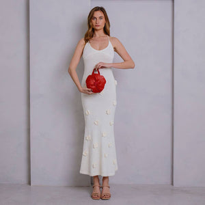 Woman in a navy dress holding a white handbag against a plain background