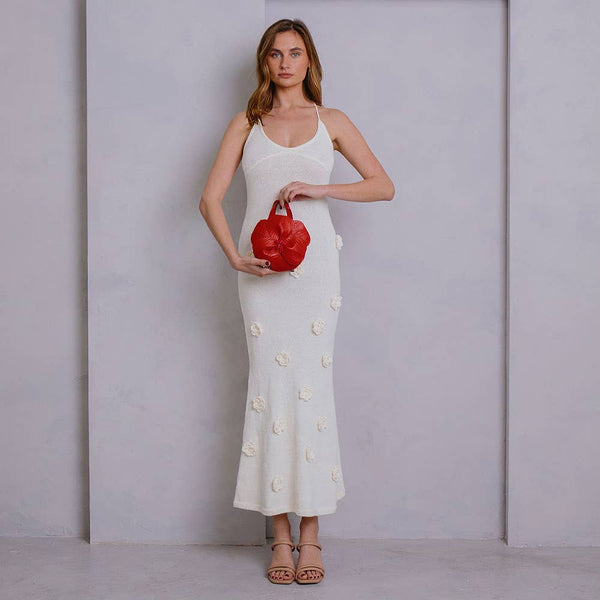 Woman in a navy dress holding a white handbag against a plain background